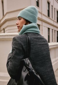 Mint green knit beanie and scarf paired with a black textured coat. The scarf is ribbed, and a black handbag with a strap is visible.