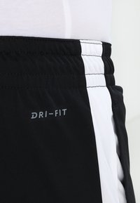 Närbild av svart och vitt sportshorts med elastisk midja och "DRI-FIT" tryckt på tyget.