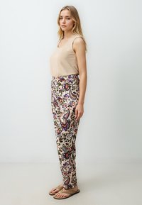 Top sans manches beige associé à un pantalon crème à motifs floraux avec des designs paisley en violet, rouge et vert. Sandales plates.