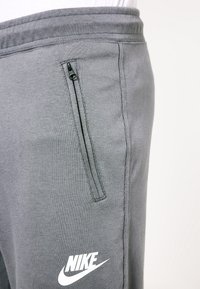 Närbild av grå Nike-sweetpants med en vertikal ficka med dragkedja och elastiskt midjeband på en person.