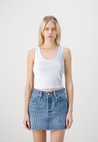 Biely rebrovaný crop top s širokým výstrihom, v kombinácii so svetlomodrou denimovou sukňou s roztrhnutými okrajmi a prednými vreckami.