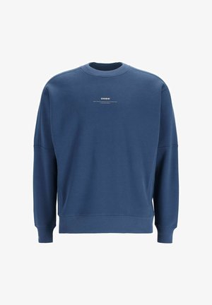 Mėlynas džemperis su apvaliu kaklu, raukšlėmis rankogaliais ir apatine dalimi. Priekyje yra mažas baltas logotipas. Pagamintas iš minkštos, tekstūruotos medžiagos.