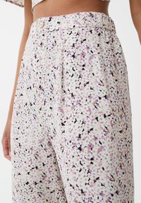 Bloemenpatroon broek in licht crème, met tinten paars en zwart, voorzien van een knoopsluiting en geplooid ontwerp. Zachte stofstructuur.