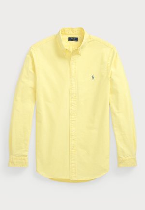 Chemise jaune à manches longues, boutonnée, avec col et petit logo brodé sur la poitrine gauche.