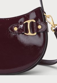 Burgundia patendi nahkustus crossbody kott kaarjate servadega, millel on kullavärvi riiv ja reguleeritav rihm. Sile ja läikiv tekstuur.