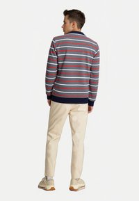 Gestreiftes Poloshirt in Grau, Rot und Weiß mit einem marineblauen Kragen. Eine beigen Hose und helle Sneakers. Lässige Rückansicht.