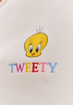 Biała tkanina z żółtą głową kreskówkowego ptaka z niebieskimi oczami i czarnymi akcentami, obok słowa "TWEETY" wyszytego w kolorowej mulinie.