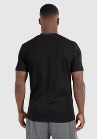 Sort bomulds T-shirt med korte ærmer, rund halsudskæring og en glat tekstur, vist fra ryggen, parret med grå shorts.