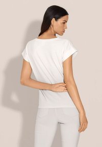 White short-sleeve t-shirt with a round neckline, smooth texture, fitted design, and subtle accent detailing on the shoulders.