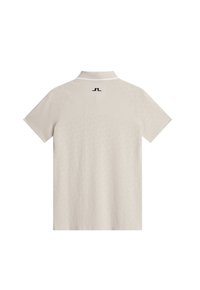 Beige polotröja med mjuk textur, korta ärmar och vit krage. Baksidan visar ett subtilt mönster och en svart logotyp.