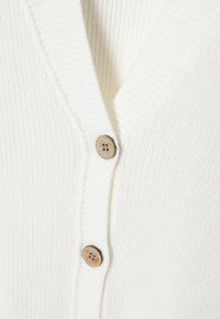 Cárdigan blanco de canalé con escote en V, botones de madera y una textura sutil en la tela. Diseño ajustado que ofrece una apariencia acogedora.