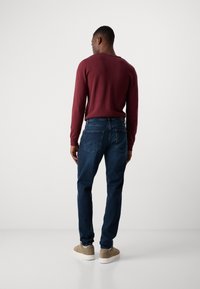 Men's outfit featuring a burgundy sweater and dark blue jeans. Sneakers are beige with a white sole. Simple design, smooth texture.