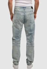 Light blue denim jeans with a tapered fit, featuring two back pockets, visible stitching, and a distressed pattern on the fabric.