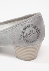 Chaussure femme en daim gris clair avec petit talon superposé et logo circulaire de la marque embossé sur le côté près du talon.