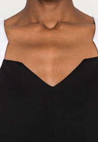 Czarny bezrękawnik z głębokim dekoltem w kształcie litery V, z kontrastującymi białymi ramiączkami. Gładka faktura, dopasowany krój i czyste linie.