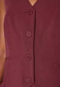 Mauve ärmelloses Top mit einem V-Ausschnitt, das vier passende Knöpfe und eine leichte Textur im Stoff aufweist, ergänzt durch eine schlichte Schneiderkunst.