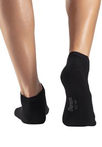 Schwarze knöchellange Socken aus gestricktem Material, mit einem gerippten Bündchen und dem Markennamen in Weiß auf der Sohle aufgedruckt.