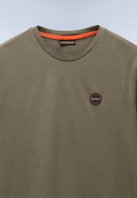 Tricou din bumbac de culoare verde măslinie, cu decolteu rotund și guler interior portocaliu contrastant, are un mic logo circular pe piept.