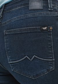 Vaqueros de mezclilla azul oscuro con un distintivo pespunte en zigzag en los bolsillos traseros, que presentan una etiqueta de marca negra y remaches de cobre.
