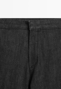 Close-up van de tailleband en bovenste sectie van zwarte denim jeans, met zichtbare stiksels en de voorkant van de ritssluiting.