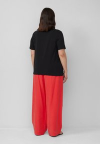 Zwarte korte mouwen t-shirt gecombineerd met wijde koraalkleurige broek. De stof is glad, met een relaxte pasvorm en een effen kleurpatroon.