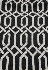 Tissu tricoté en noir et blanc avec un motif géométrique répétitif de formes hexagonales et ovales entrelacées.
