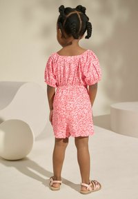 Rosa Blumenspritzer mit Puffärmeln, elastischem Bund und Shorts. Bietet einen strukturierten Stoff und wird mit leichten Sandalen kombiniert.