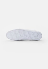 Semelle de sneaker blanche avec motif de bande de roulement circulaire et logo "Lacoste" embossé près du talon sur un fond blanc uni.