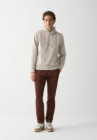 Světle šedá mikina s kapucí a stahovacími šňůrkami, v kombinaci s vínovými kalhotami a bílými teniskami se béžovými a hnědými akcenty. Hladká textura.