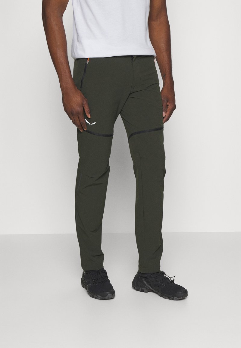 Zielone oliwkowe spodnie cargo z zamykanymi kieszeniami, slim fit, z kontrastowym czarnym przeszyciem z przodu. Noszone z białym t-shirtem i czarnymi butami.