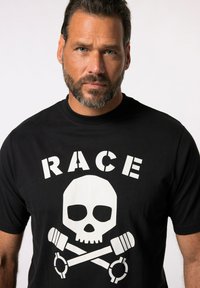 Sort T-shirt med et hvidt grafisk design med ordet "RACE", et skelet og krydsede skruenøgler, placeret centralt på forsiden.
