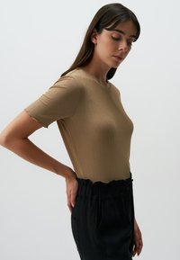 Bruine geribbelde t-shirt met korte mouwen en een gegolfde halslijn, gecombineerd met zwarte high-waisted broek met een gepofte tailleband en zakken.