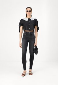 Melnā cropped top ar izpušķotiem piedurknēm un baltu mežģīņu apkakli, apvienots ar augsto jostasvietu melnajām džinsēm un siksniņām sandālēm. Tur melnu somu.