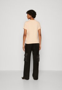 Perzikkleurige t-shirt met korte mouwen, relaxte pasvorm, gecombineerd met zwarte cargobroeken met twee zijzakken, een zachte textuur en wijde pijpen.