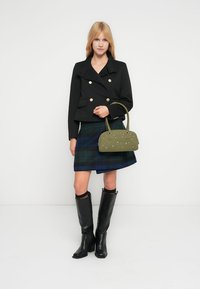 Μαύρο παλτό peacoat με χρυσά κουμπιά, καρό φούστα σε πράσινους και μπλε τόνους, τσάντα ώμου χακί με ασημί τρουκ, μαύρες μπότες με τακούνι μέχρι το γόνατο.