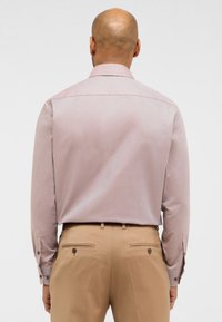 Camicia da dress leggera di colore rosa chiaro, con colletto e polsini abbottonati, abbinata a pantaloni beige con tasche posteriori e dettagli con bottoni.