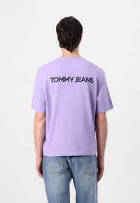 Lavender cotton T-shirt with a loose fit. The back features "TOMMY JEANS" in bold black lettering. Paired with light blue denim jeans.