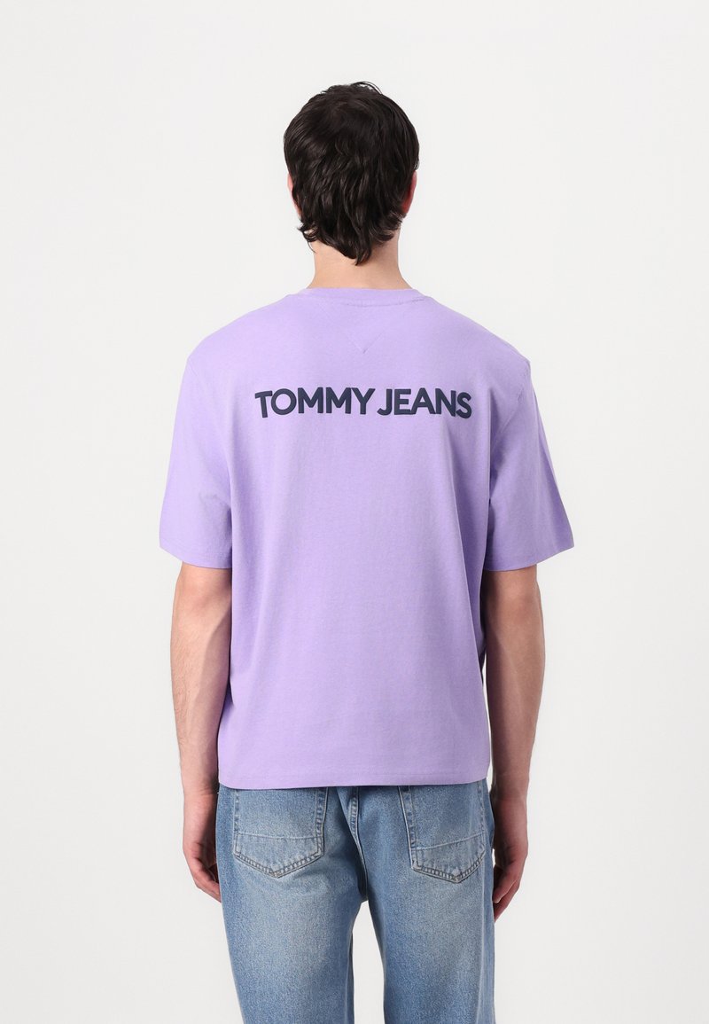 Lavender cotton T-shirt with a loose fit. The back features "TOMMY JEANS" in bold black lettering. Paired with light blue denim jeans.