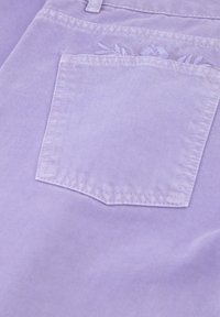 Lila denimstof met een gestikte achterzak met bloemembroidery. De textuur is glad met een subtiele glans.