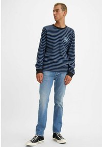 Camisa de manga larga a rayas azules y negras con cuello redondo, combinada con jeans azul claro y zapatillas de lona negras.