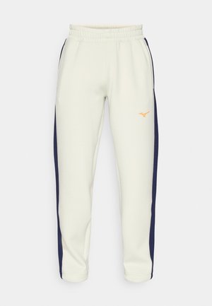 Lys beige joggebukser med snor i livet, marineblå sidestriper og en oransje logo på venstre lår; laget av mykt materiale.