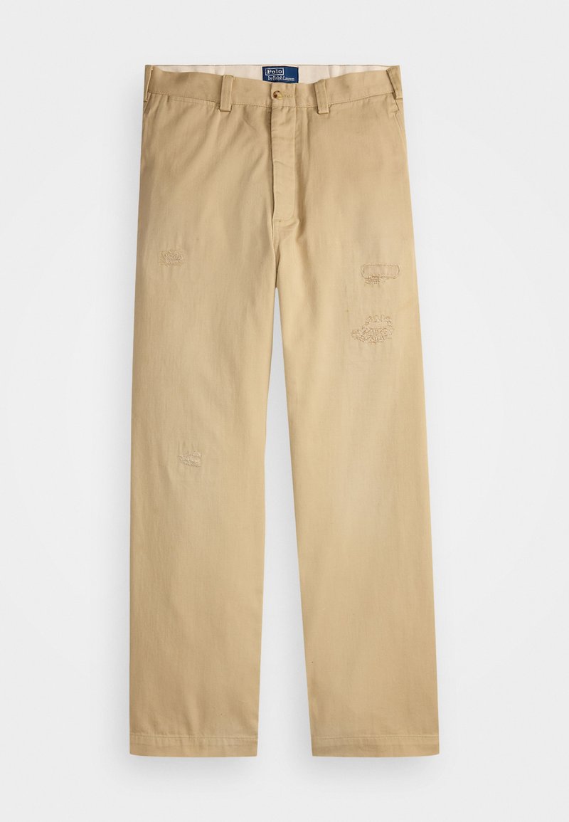 Pantalones de algodón beige con corte recto. Presentan parches desgastados y detalles de bordado en la parte delantera. Cierre clásico con botón y cremallera.