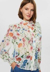 Blommig blus i ett genomskinligt, lätt tyg, med livfulla rosa, orange och blå blommor, rynkad krage och åtsittande ärmslut.