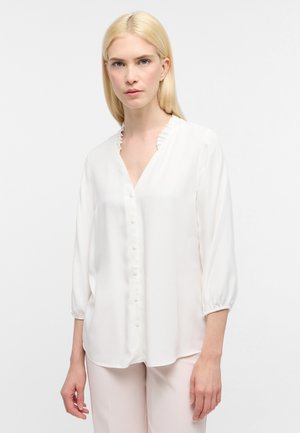 Witte blouse met een V-hals, ruffles aan de randen en knoopsluiting. Heeft driekwartmouwen met een losvallende pasvorm en een gladde textuur.