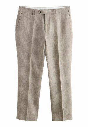 Muž stojaci na kamenných schodoch, oblečený v hnedých nohaviciach s prúžkami a modrej košeli s krátkym rukávom, smerujúci k bielej štruktúrovanej stene.