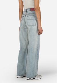 Világoskék, bő szárú farmernadrág, magas derékkal, két hátsó zsebbel és kontrasztos címkével a hátsó részén.