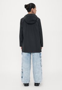 Black hooded jacket with a smooth texture, long sleeves, and a straight cut, paired with light blue wide-leg cargo pants featuring pockets.