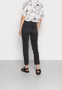 Svarta denimjeans med en avsmalnande passform, som har bakfickor och en lätt blekning. Kombineras med en grafisk t-shirt med kort ärm och svarta sandaler.