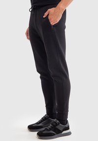 Pantalones jogger negros hechos de tejido ligero, con bolsillos laterales con cremallera, dobladillos ajustados y una cinturilla con cordón para un ajuste ajustable.
