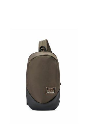 Kompaktowy, oliwkowozielony i czarny plecak na jedno ramię z jedną ramiączkiem i naszywką z napisem „Ochnik Riders Supply Custom Built” na przodzie.